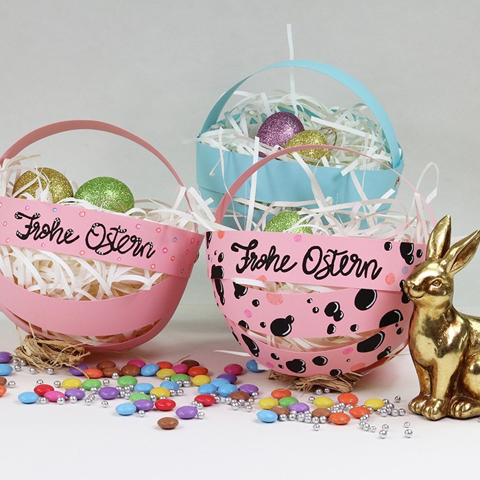 pastellfarbene Osterkörbchen mit Eiern, Schokolinsen und Goldhase